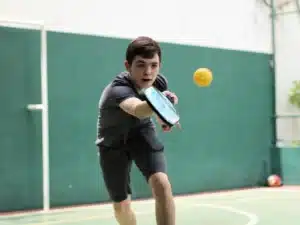 A boy trying to hit a ball with his pickleball paddle
